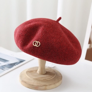 Close-up of red wool beret with golden double-ring buckle detail and soft texture