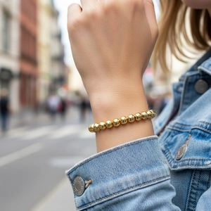 Detail of 18K gold-plated beaded elastic bracelet worn with a blue denim jacket