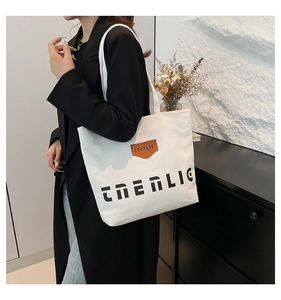 Detail of white canvas tote bag with black lettering and leather patch on model shoulder