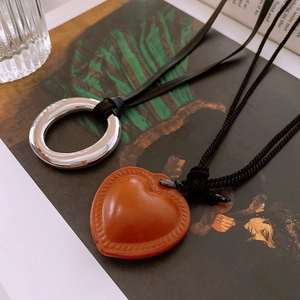 Detail of silver geometric ring and brown faux leather heart pendant on black cord necklace