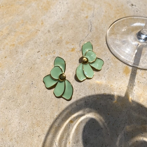 Detailed view of mint green enamel flower earrings with gold metal edges on stone