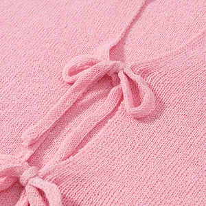 Detailed close-up of pink knit top featuring a delicate ribbon bow tie and textured fabric