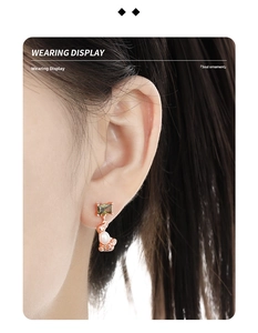 Close-up of elegant gold earrings with green square gemstone and baroque pearl