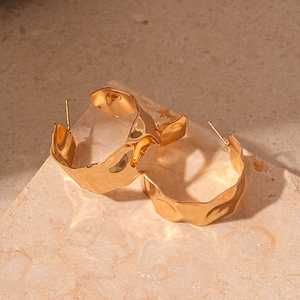 Close-up of golden chunky hoop earrings with hammered texture on natural stone
