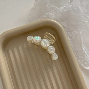 Macro detail of a large acrylic hair claw clip with faux pearls on a beige tray