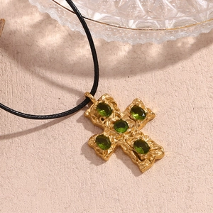 Macro view of golden hammered cross pendant with five green gems and black cord necklace