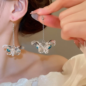 Close-up of transparent butterfly earrings with blue accents and gold chain on model