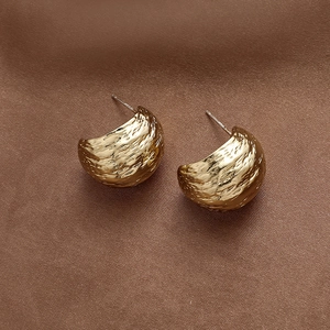 Close-up of golden dome earrings with hammered metal texture on brown silk background