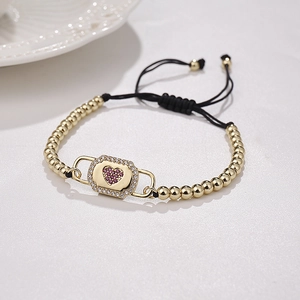 Detail of adjustable gold bead bracelet with purple zircon heart and black cord