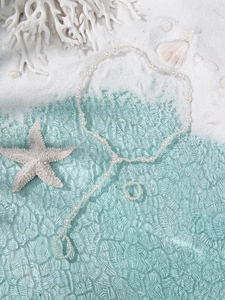 Flat lay of white pearl necklace and ring set on beach sand with starfish decor