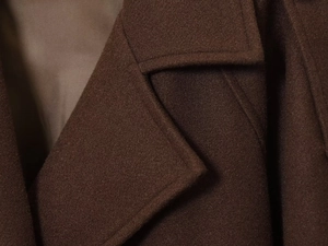 Macro shot of dark brown wool coat lapel showing premium fabric texture and stitching