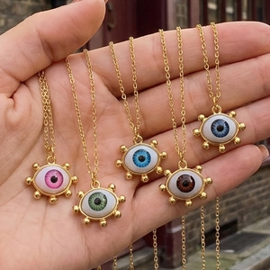 Detail of five colorful Evil Eye necklaces with gold plating held in hand over a street view