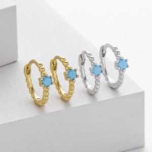 Detail of gold and silver beaded earrings with blue round center stones on a white stand