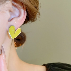 Gros plan d'une boucle d'oreille cœur jaune avec bord doré portée sur une oreille