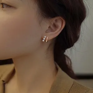 Close-up of minimalist gold bar and triple pearl earrings worn on a model's ear