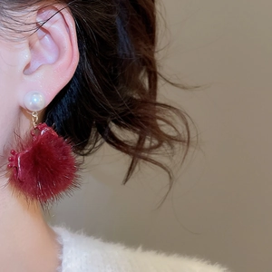 Close-up of a model wearing red plush ball earrings with pearls and golden accents