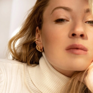 Close-up of golden textured earring set and ear cuff on model with white sweater