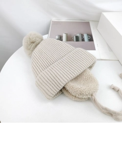 Detailed view of beige knit baby hat with warm fleece lining and fuzzy pom-pom detail