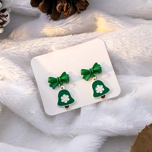 Christmas earrings featuring a green bow and snowflake bell on a cozy winter background