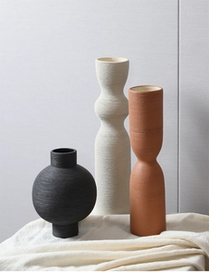 Close-up of matte textured ceramic vases in black, off-white, and brick red colors