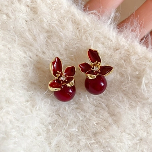 Macro detail of red enamel flower earring with dark red pearl drop on white fabric