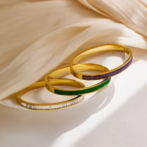 Close-up of gold-plated bangles with purple, green and white rectangular gemstones on silk