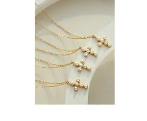 Close-up of four golden cross necklaces with white pearls on a minimalist white display