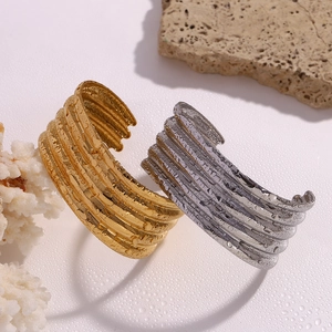 Detailed view of layered wavy open bangles with water droplets on gold and silver finish