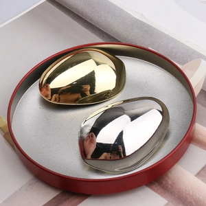 Polished metallic egg-shaped hair clips in gold and silver set on a decorative red tray
