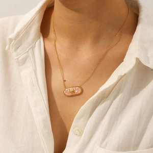 Detail of a pink shell pendant with gold motif on a thin chain worn by a model