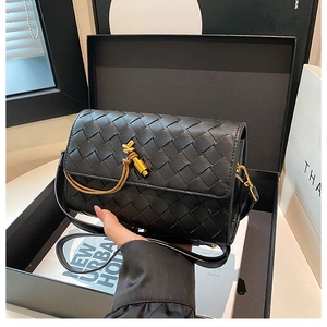Detail of hand-woven black leather bag with a golden knot clasp and slim shoulder strap