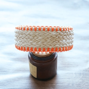 Close-up of beige woven raffia bracelet with orange stitched edges on a glass jar