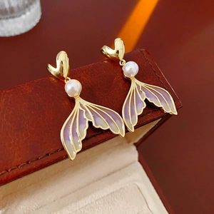 Gold heart stud earrings with purple enamel mermaid tails and pearls on a leather box