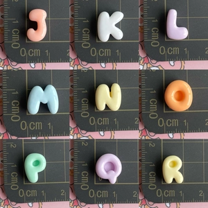 Mini resin alphabet charms J-R in grid layout on measuring mat for DIY hair accessories