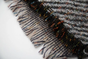 Detail of grey herringbone fabric texture and colorful fringe tassels on scarf