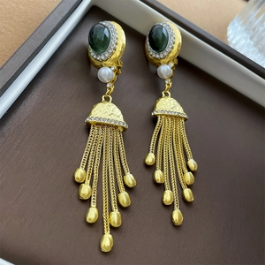 Gros plan détaillé de boucles d'oreilles vintage à pompons dorés avec pierre verte et perle