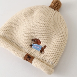Détail du bonnet tricoté pour bébé avec broderie chiot et pompon en laine douce