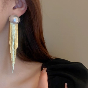 Close-up of elegant gold tassel earrings with a large round white pearl on a model