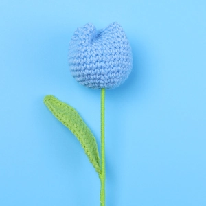 Detailed close-up of a handcrafted blue crochet tulip flower with green stem and leaf