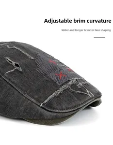 Détail de la casquette plate en jean gris avec bord pliable et broderie X rouge