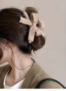 Close-up of a plush oversized knit bow hair claw clip in beige on a woman's hair