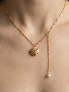Détail du collier pendentif cœur doré avec texture tressée et accent de perle blanche