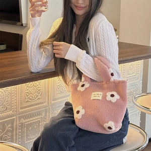 Detail of pink plush tote bag with white flower patterns and branding label in use