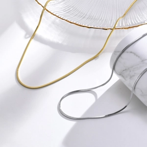 Minimalist square snake bone necklaces in gold and silver finish on white marble pedestal
