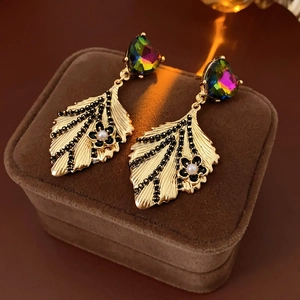 Detail view of golden leaf earrings with black stones and a central pearl on velvet box