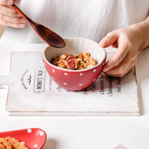 Cute red ceramic mushroom bowl with white dots holding cereal and a wooden spoon