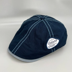 Detailed side view of navy blue flat cap with blue stitching and embroidered label