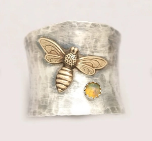 Macro detail of silver hammered ring featuring brass bee and iridescent opal stone