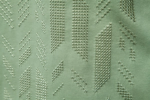 Macro shot of green knitted fabric with precise cross-stitch embroidery on slim-fit T-shirt