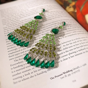 Detailed close-up of emerald green crystal tassel earrings on a vintage book page